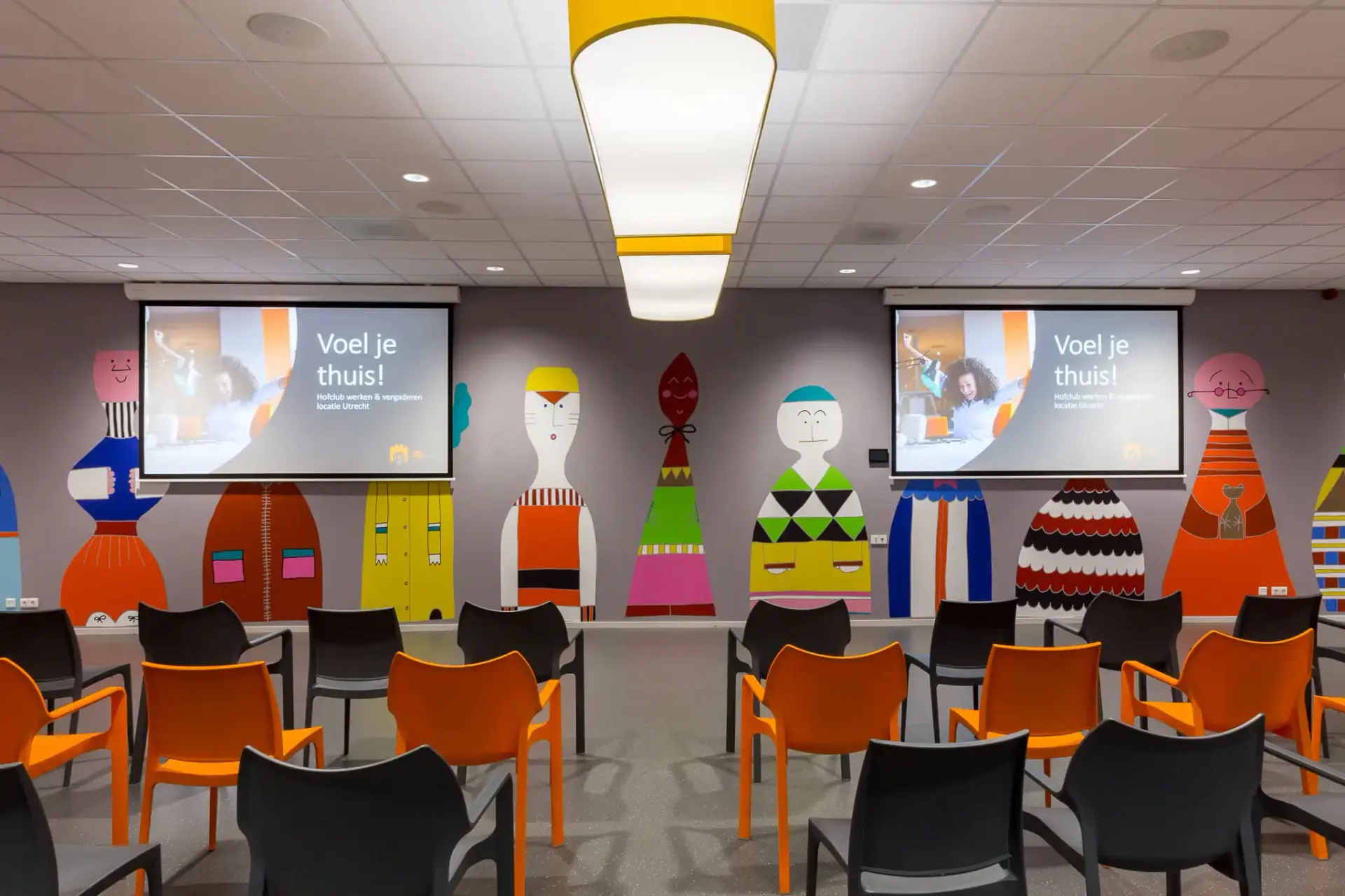 Zaal in theateropstelling met twee schermen en gekleurde wanddecoratie