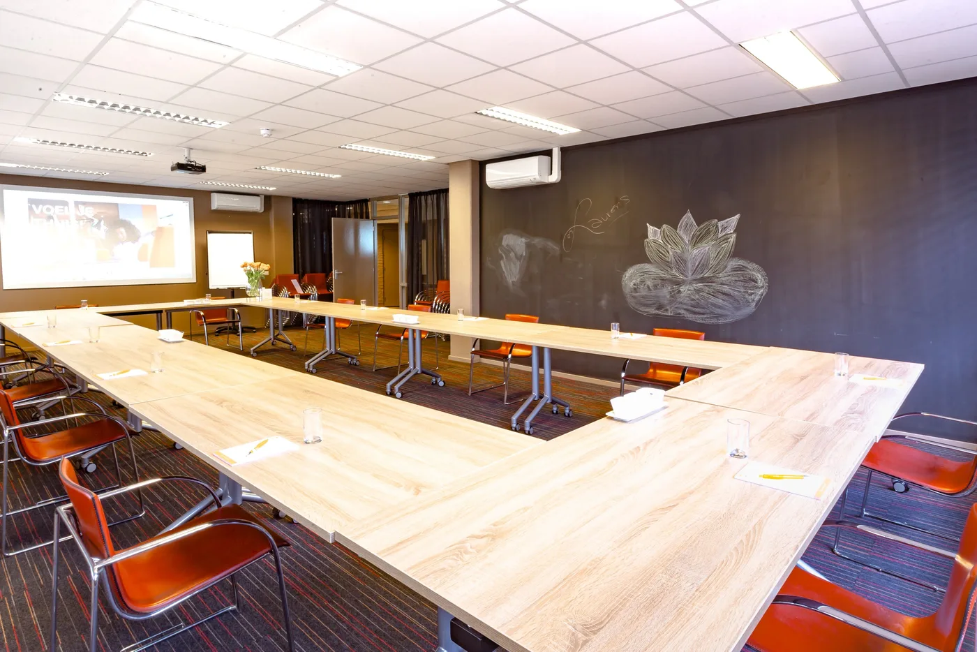 Vergaderzaal met tafels in U-opstelling en een groot scherm