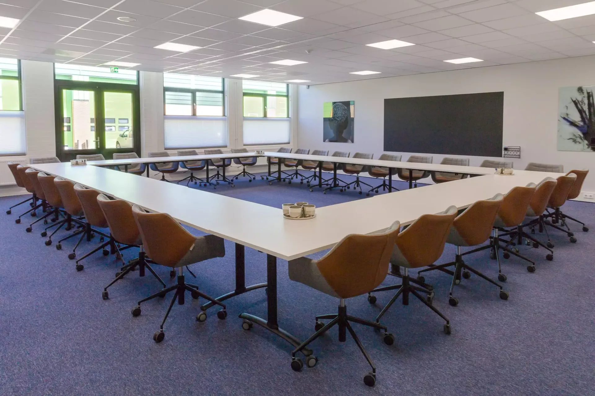 Vergaderzaal met tafels in blokopstelling en stoelen eromheen